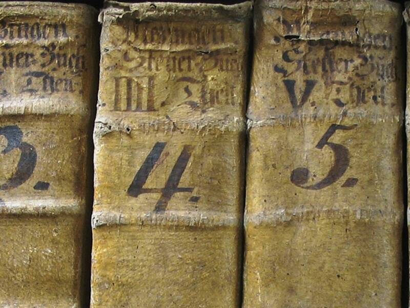 Buchrücken von alten Büchern sind nebeneinander aufgereiht. Die Buchrücken sind von 1 bis 7 durchnummeriert.
