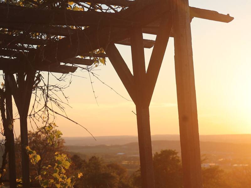 Eine Sonnenuntergangsituation in der Natur, zu sehen sind Sonne und ein Holzüberstand mit Ausblick in die Weite über Metzingen.