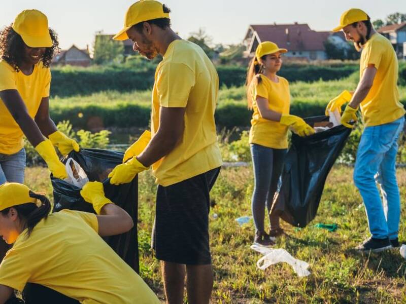 Hier sind Menschen zu sehen, die gelbe Kleidung an haben und Müll sammlen.