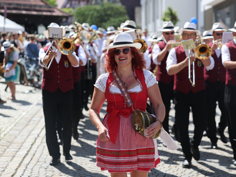 Stadt- und Heimatfest 2025 in Metzingen. Eine Vereinsgruppe vom Umzug ist zu sehen, die Frau in Tracht und im Hintergrund Personen mit Blasinstrumenten.