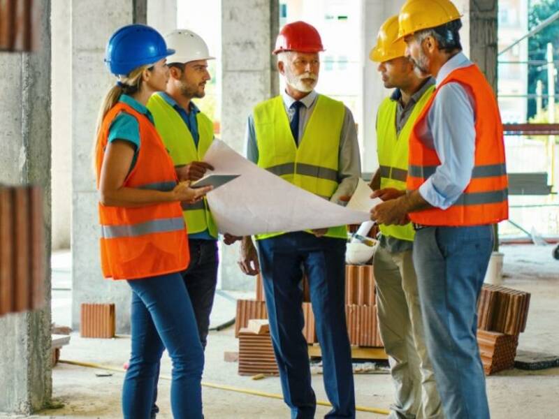 Hier ist einen Gruppe von arbeitenden zu sehen, die in einem Haus stehen, das noch gebaut wird. Sie besprechen etwas. 