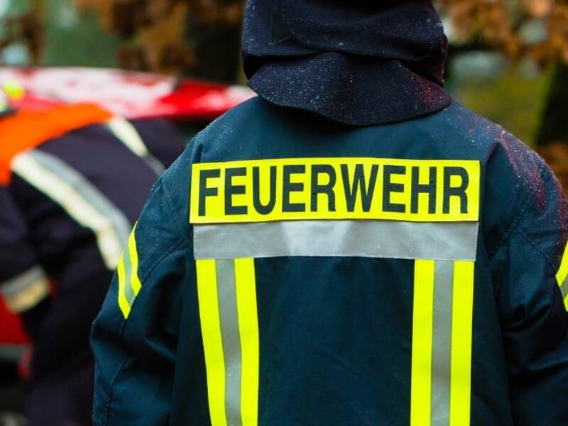 Hier ist ein Feuerwehrmann von der Rückseite zu sehen. Auf seinem Rücken der Arbeitskleidung steht "Feuerwehr".