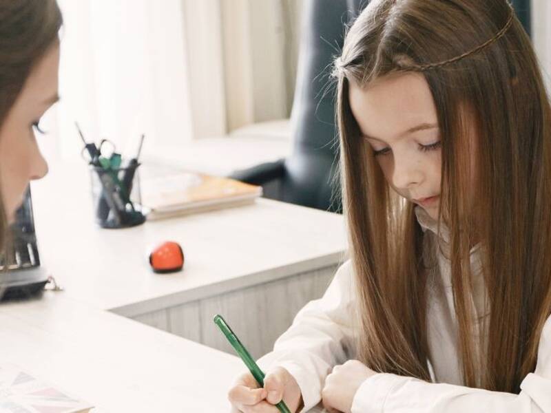 Hier ist eine Frau zu sehen, die Kindern bei den Hausaufgaben hilft. 