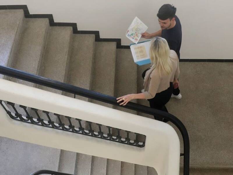Hier ist ein Treppenaufgang zu sehen. Dieser ist im Alten Rathaus in Metzingen und auf der Trepp gehe gerade zwei Mitarbeitende hoch. 