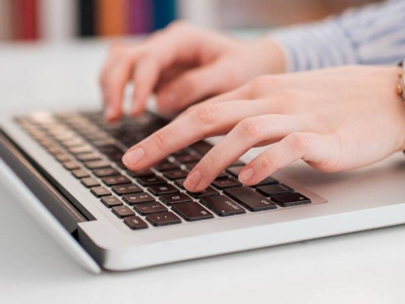 Hier ist ein Laptop zu sehen und zwei Hände, die auf der Tastatur schreiben. 