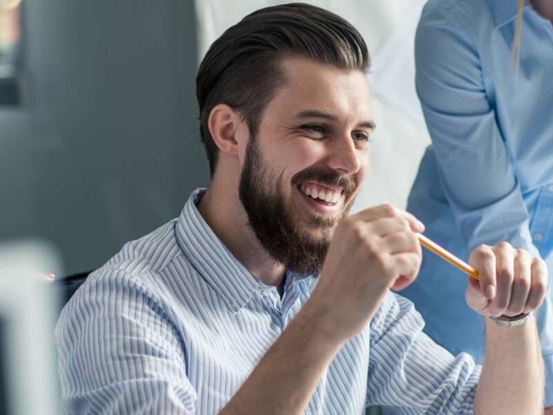 Hier ist eine Mann zu sehen, der auf einem Bildschirm schau und einen Stift in der Hand hat. Hinter ihm stehen zwei Frauen und schauen mit auf den Bildschirm.