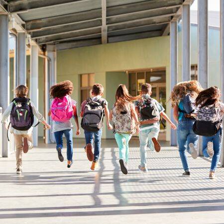 Hier sind Schüler in einer Gruppe nebeneinander, von hinten zu sehen, die in einem Schulhaus springen. 
