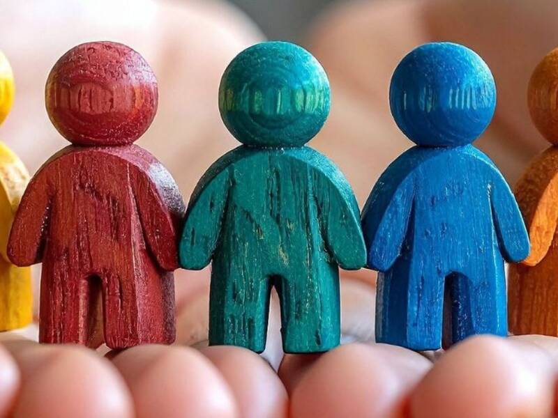 Hier sind zwei Hände zu sehen. Auf diesen stehen bunte Holzfiguren. Sie symbolisieren ein Gefühl von Zusammenhalt und Gemeinschaft. 