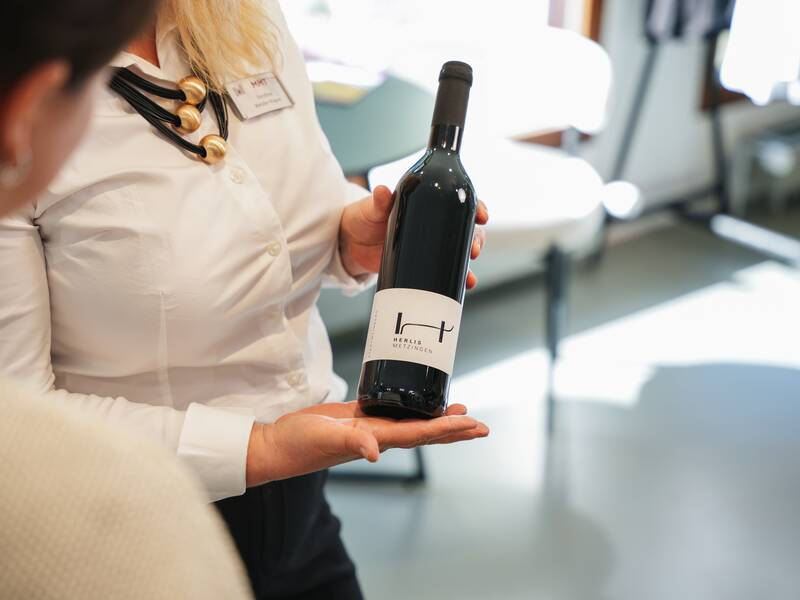 Eine Mitarbeiterin der MMT Metzingen präsentiert gegenüber einer Kundin eine Flasche Wein.