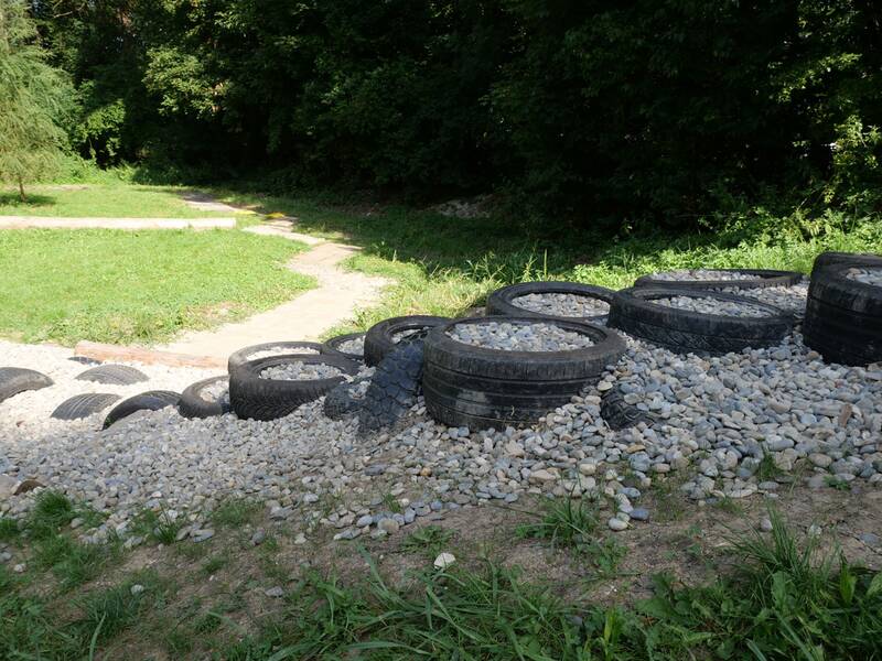 Mehrere alte Autoreifen, gefüllt mit Kieselsteinen, liegen als Hindernis auf einem Barfußpfad.