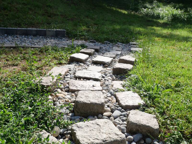 Ein Weg aus großen, unregelmäßigen Steinplatten ist von Kieselsteinen umgeben.