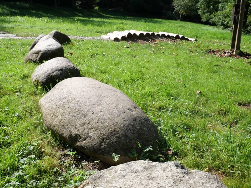 Eine Reihe großer, runder Findlinge liegt als Trittsteine im Gras.
