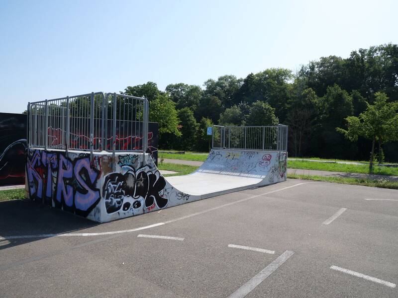 Halfpipe mit Graffiti an den Seiten, dahinter Bäume und Wiese.