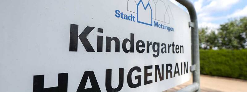 Ein Schild am Zaun zeigt den Schriftzug "Kindergarten Haugenrain" mit dem Logo der Stadt Metzingen.