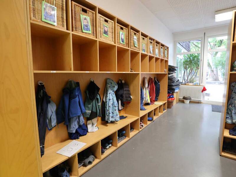 Garderobe: Holzeinbauten mit Körben und Kinderfotos, darunter kleine Fächer mit Jacken und Schuhen.