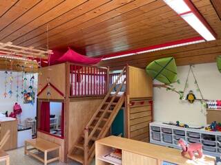Das Bild zeigt einen liebevoll eingerichteten Kindergartenraum mit einer Holzkonstruktion zum Klettern, bunten Dekorationen und Aufbewahrungskisten für Spielzeug.