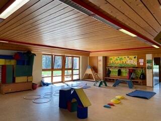 Ein heller Raum mit Holzboden und -decke ist ausgestattet mit bunten Spielgeräten und Matten, ideal für Kinderaktivitäten.