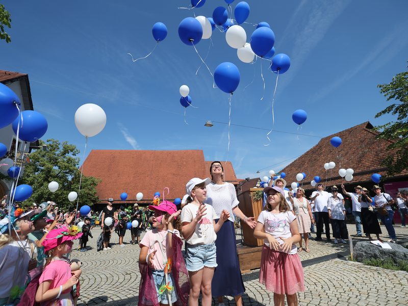 Stadt- und Heimatfest 2025 im Juli in Metzingen. Weiße und blaue Luftballons steigen in den blauen Himmel. Zu sehen sind Oberbürgermeisterin Carmen Haberstroh und Kinder, die lachend in den Himmel schauen.