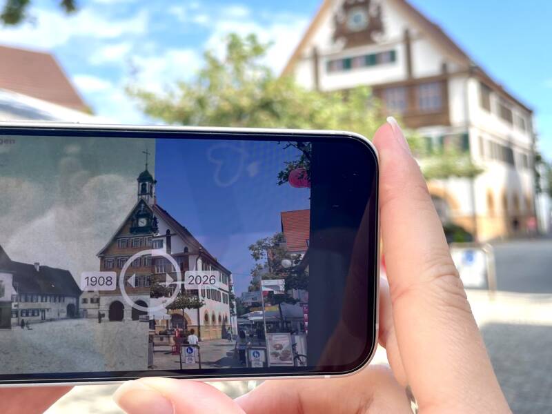Smartphone im Vordergrund zeigt die Future History Tour von Metzingen, das Rathaus im Hintergrund