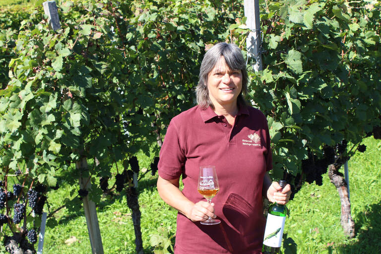 Elisabeth Eberle Eine Person steht in einem Weinberg und hält ein Glas Weißwein und eine Weinflasche in den Händen.
