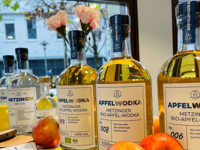 Eine Sammlung von Getränkeflaschen mit Bio-Apfel-Wodka und Gin steht auf einem Tisch, dekoriert mit frischen Äpfeln und einer Zitrone im Vordergrund.
