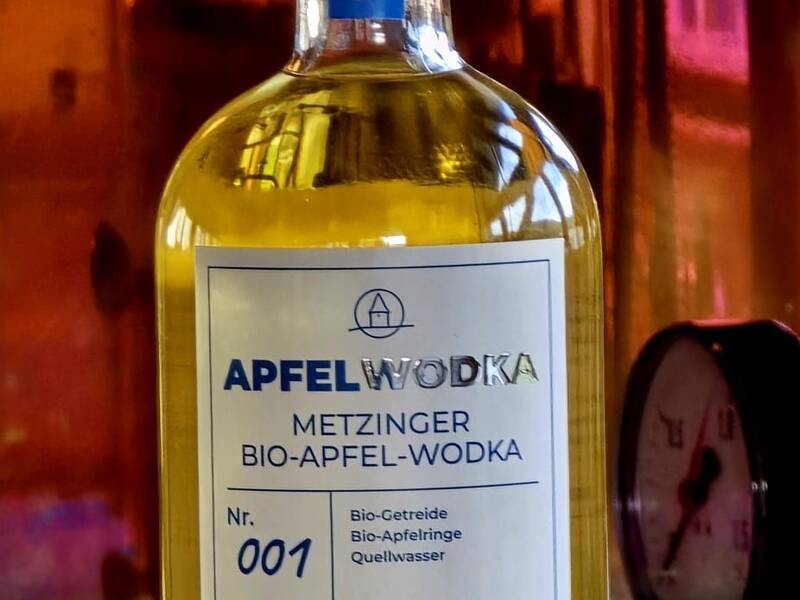 Eine Flasche Bio-Apfel-Wodka mit 40% Alkoholgehalt steht vor einem verschwommenen Hintergrund und hat ein Etikett mit der Aufschrift "Metzinger Bio-Apfel-Wodka".