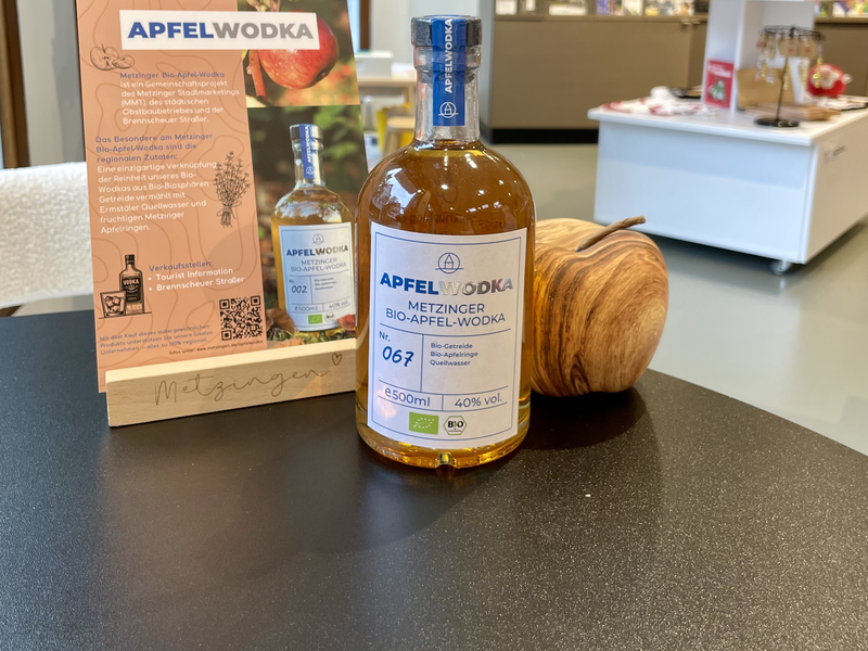 Eine Flasche Metzinger Bio-Apfel-Wodka steht auf einem Tisch in einem Verkaufsraum, umgeben von Produktinformationen und Dekorationen.