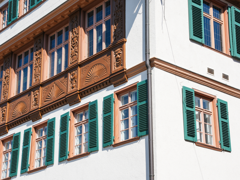 Ein Teil eines Gebäudes mit weißen Wänden und großen Fenstern, die braune Verzierungen und grüne Fensterläden haben.