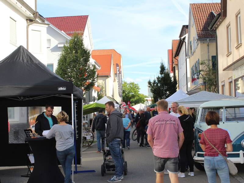 Ein belebter Straßenmarkt mit Menschen, die an Ständen und einem blauen Retro-Bus vorbeischlendern.