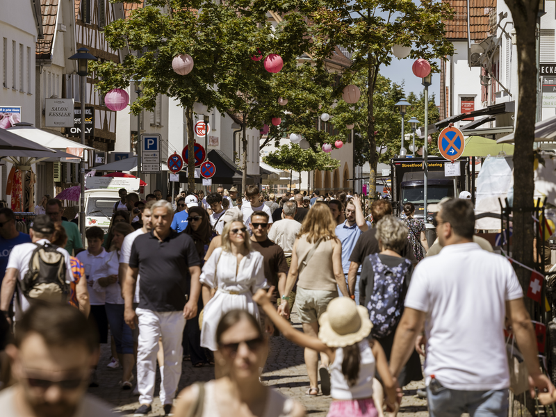 Eine belebte Einkaufsstraße mit vielen Menschen und Dekorationen in Form von bunten Papierlaternen an den Bäumen.