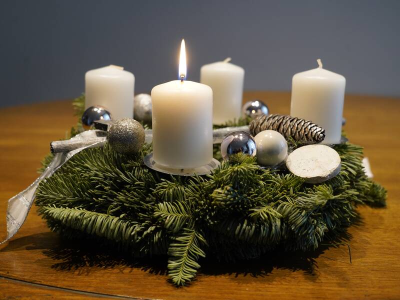 Adventskranz mit weißen Kerzen, die erste Kerze brennt.
