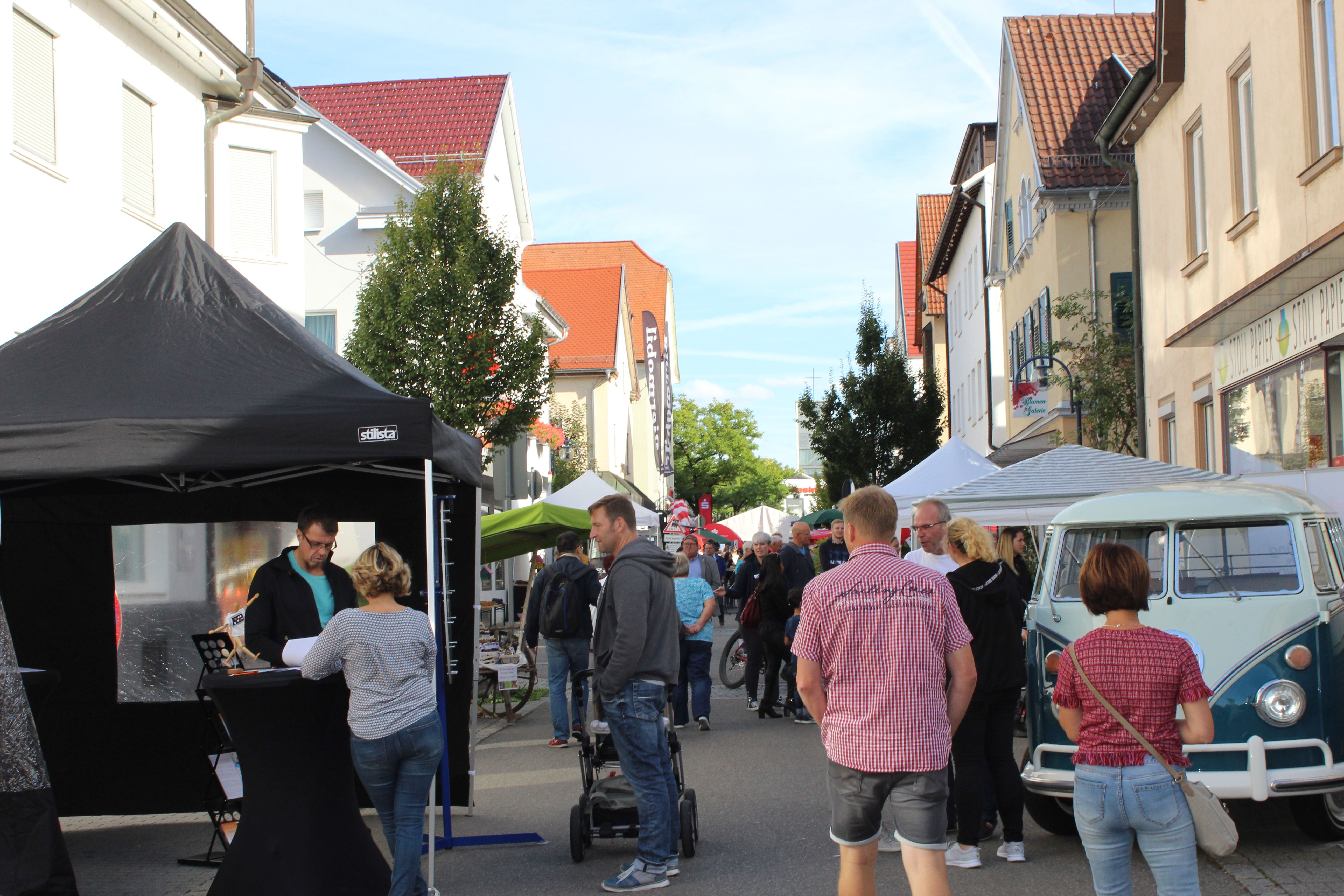 Ein belebter Straßenmarkt mit Menschen, die an Ständen und einem blauen Retro-Bus vorbeischlendern.